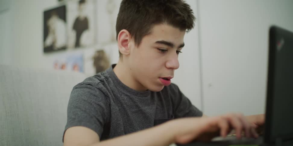 A boy sitting and typing on a laptop
