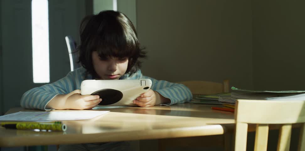 A boy sitting at a table looking at a tablet