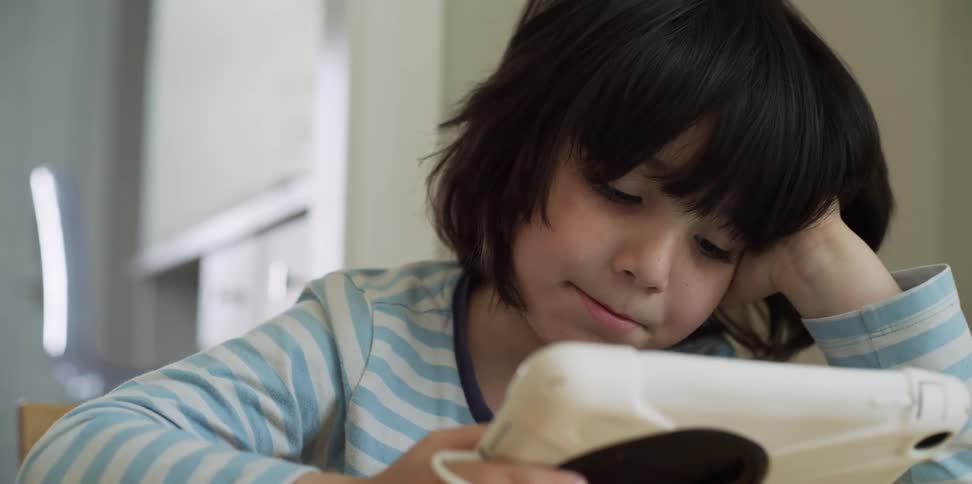 Child sits leaning head on hand while watching tablet