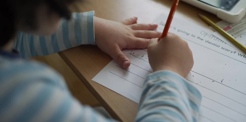 Girl doing homework with paper and pencil on a table at day