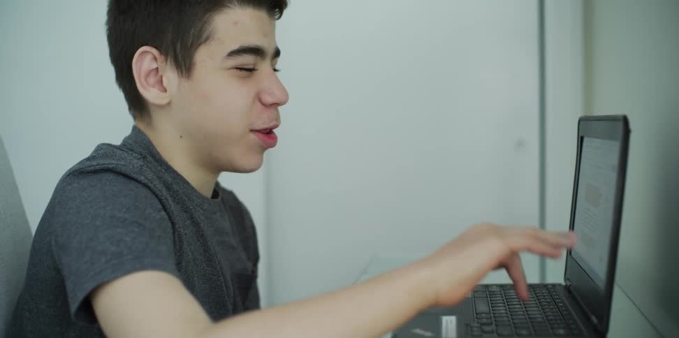 A boy sitting and talking while on a laptop