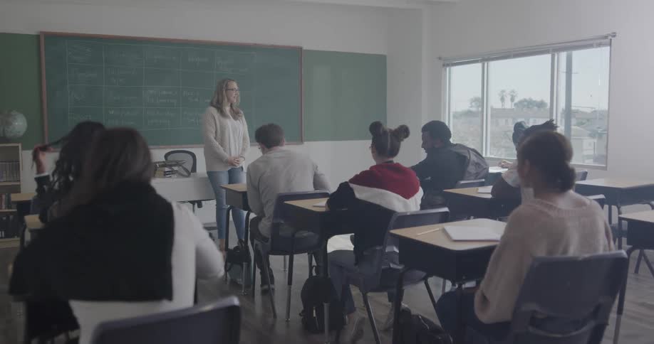 Students sit and chat in their desks until a teacher walks in and starts talking to them