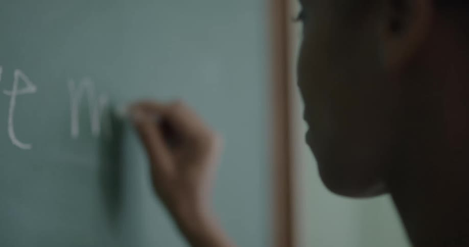 A teenage girl writes on a chalkboard in a classroom