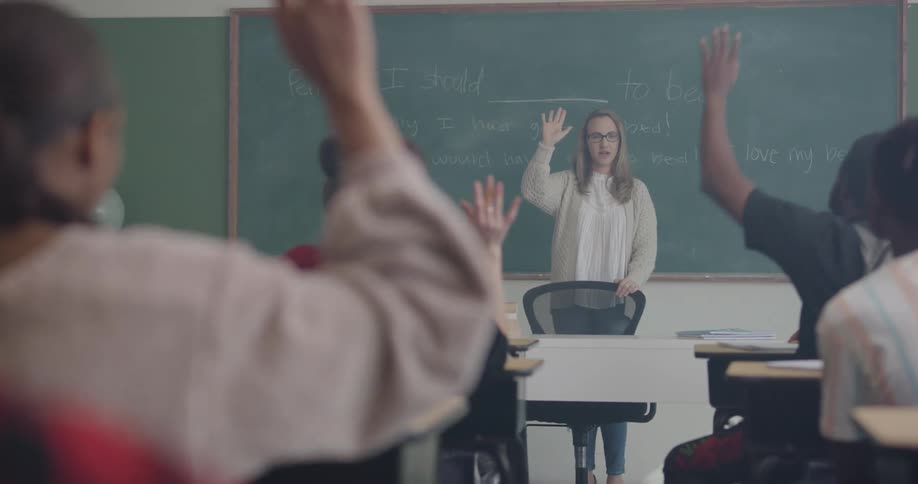 A teacher and students raising their hands in a classroom