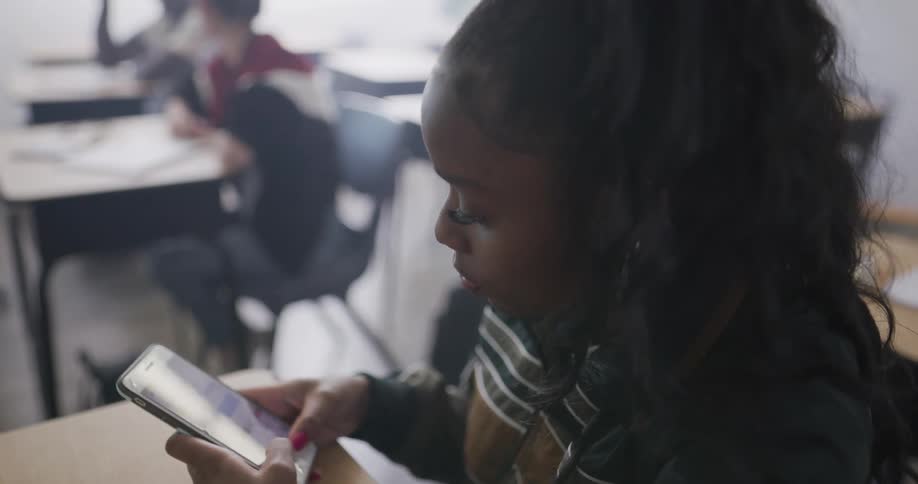 A girl sits in her desk and texts on her phone
