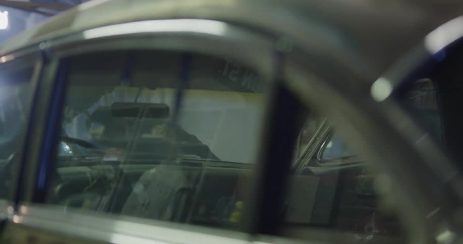 A mechanic works under the hood of a car shining a light on the engine in a garage