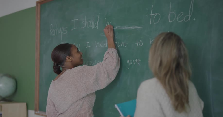 Teacher talking to student in front of blackboard in classroom