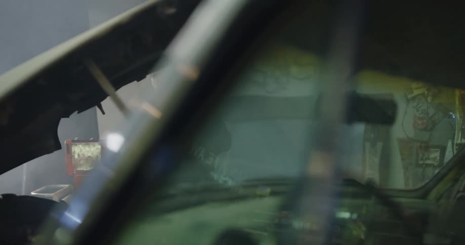 A mechanic gets a tool from his tool box and begins working under the hood of a car