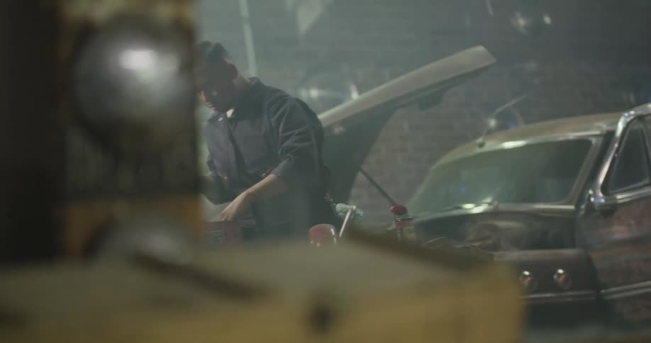 A mechanic gathering tools then working underneath a car hood