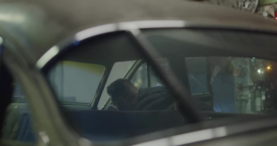 A mechanic in the garage opening up a car door and the car hood