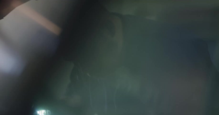 A mechanic holds a work light and examines the engine under the hood in a garage