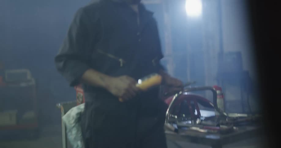 A man walks to his tool box and picks up a tool and a work light then returns to the car he is repairing
