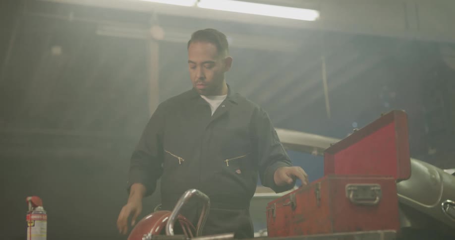 A mechanic in a garage places his tools back into his toolbox and closes it