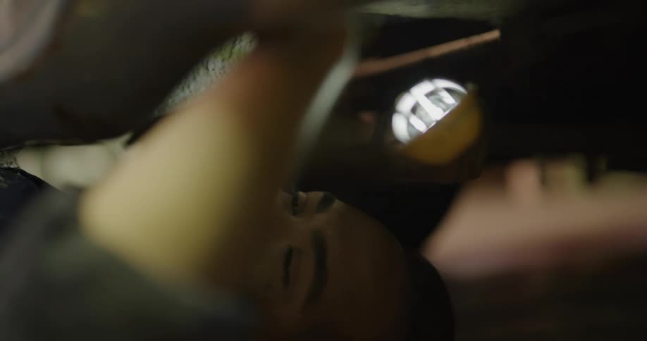 A mechanic lies underneath a car and holds a light as he works