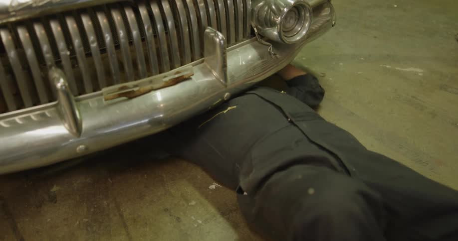 A mechanic in a garage laying on the floor working underneath a car