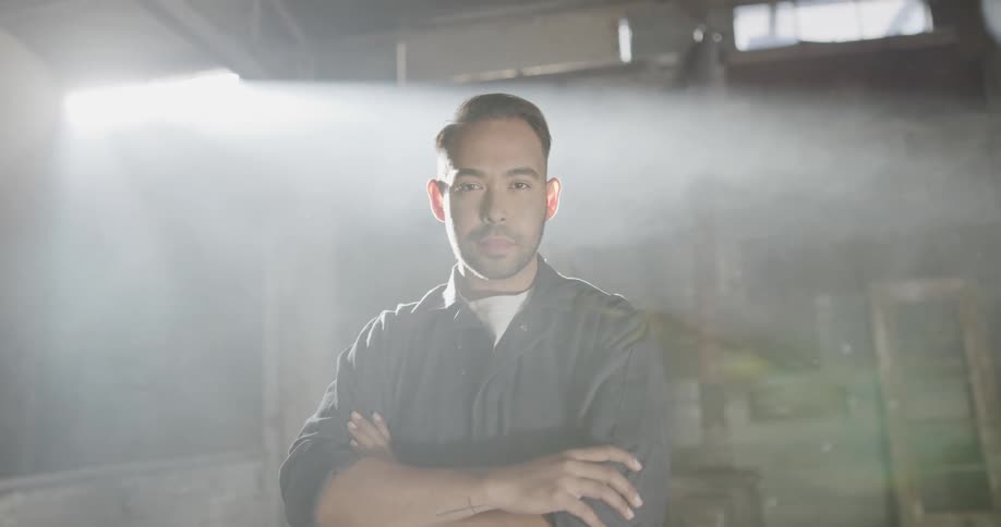 A man stands in a smoky room and looks around with his arms crossed over his chest