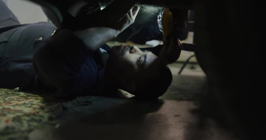 A male mechanic lays on the ground while working on a vehicle