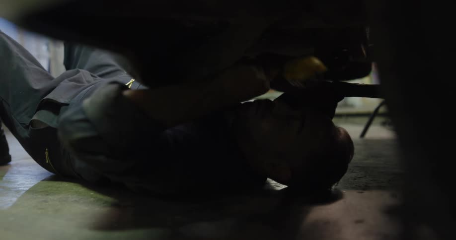 A mechanic works underneath a car while holding a light