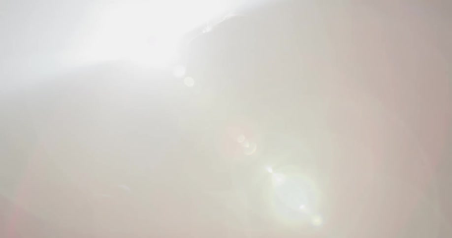 A man stands smiling with a light shining behind him causing glare