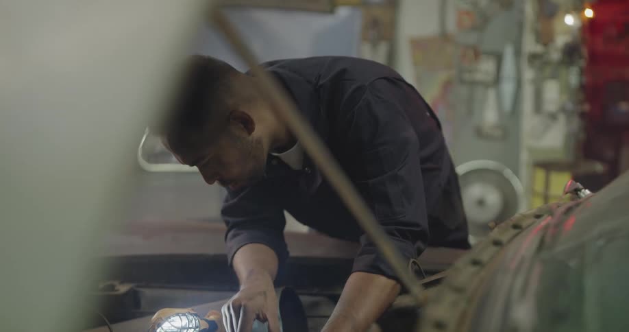 Mechanic works on vintage car engine in workshop