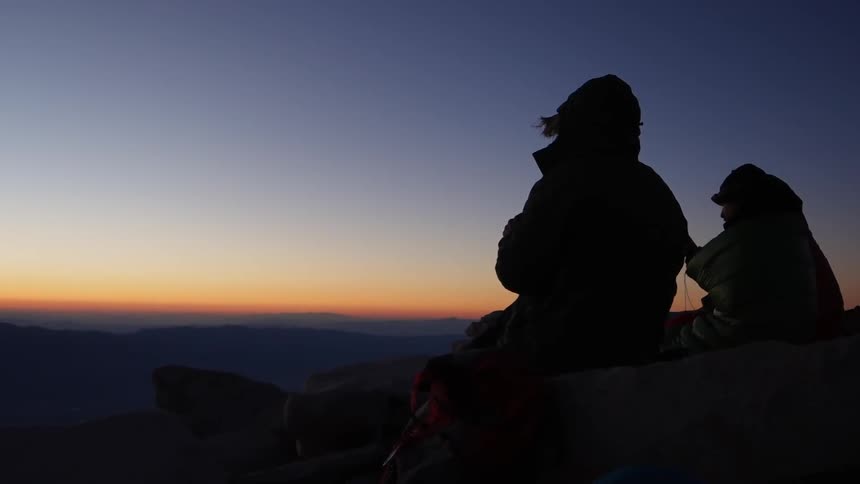 People sitting on rocks watch the sunset