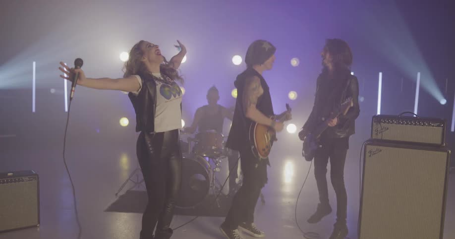 A group of musicians jump and sing and play instruments on stage