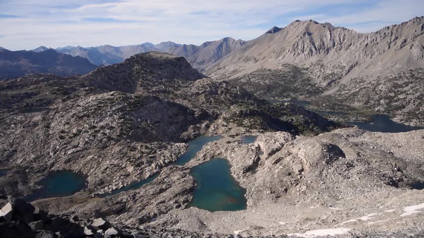 Many mountains covered in dirt with pools of water scattered about on a bright but cloudy day