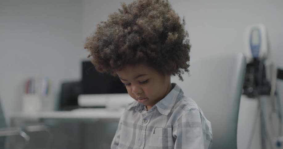 Black toddler boy sits in a chair in a clinic
