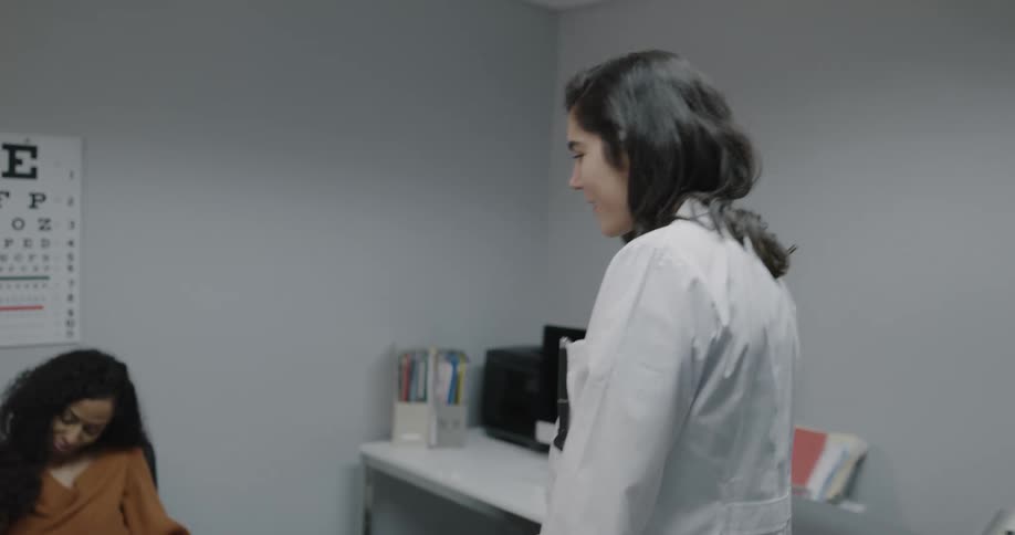 A doctor places her stethoscope around her neck as she walks to an exam room where she greets a waiting mother and son