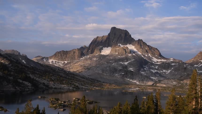 Aerial footage of a body of water at the foot of mountains with patches of snow on them