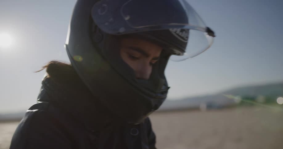 A person takes off their protective gear while sitting on a motorcycle in the desert