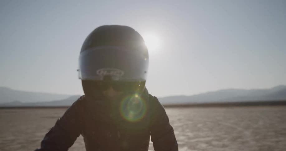 A motorcyclist puts on sunglasses and lowers her helmet before riding in the desert