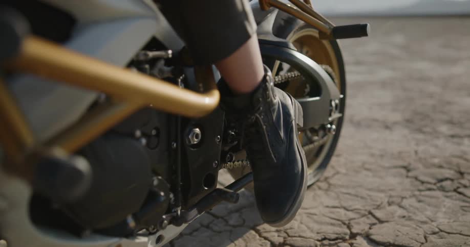 A woman stepping on shift pedal of a motorcycle before driving off through a desert