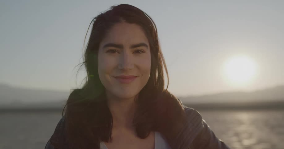 A woman in the desert takes off here sunglasses while looking into the camera then looks off in the distance