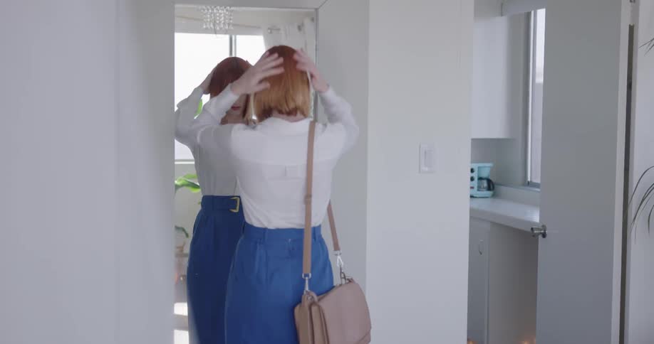 Red haired woman looks in the mirror and checks appearance at home