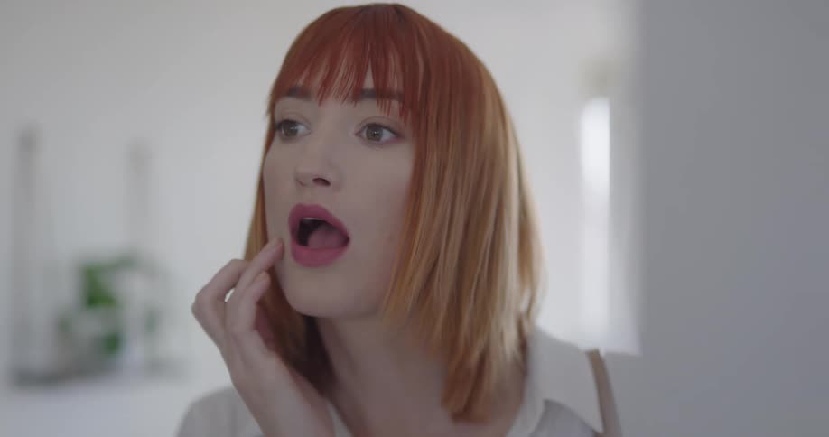 A redheaded woman checks her hair and lipstick before leaving the house
