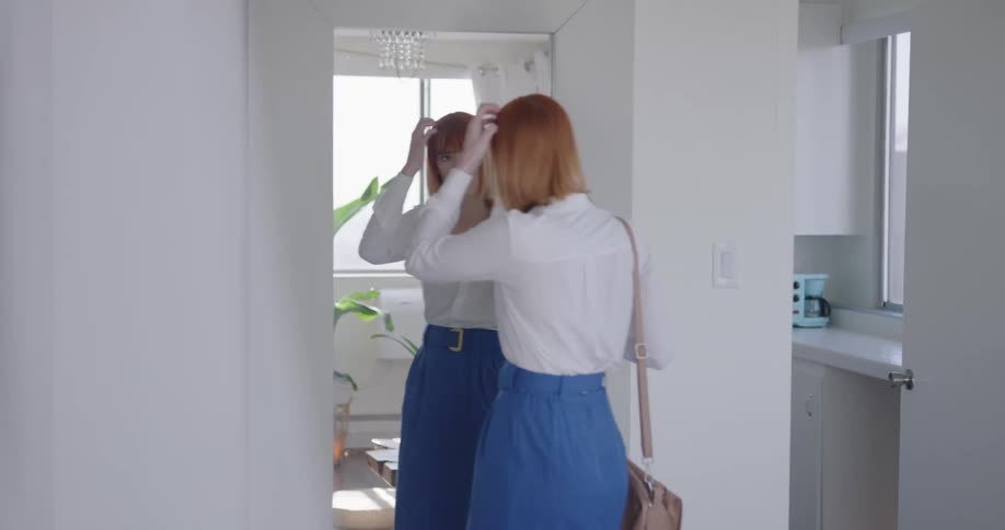 Red headed woman looks in the mirror and checks her appearance before going out at home