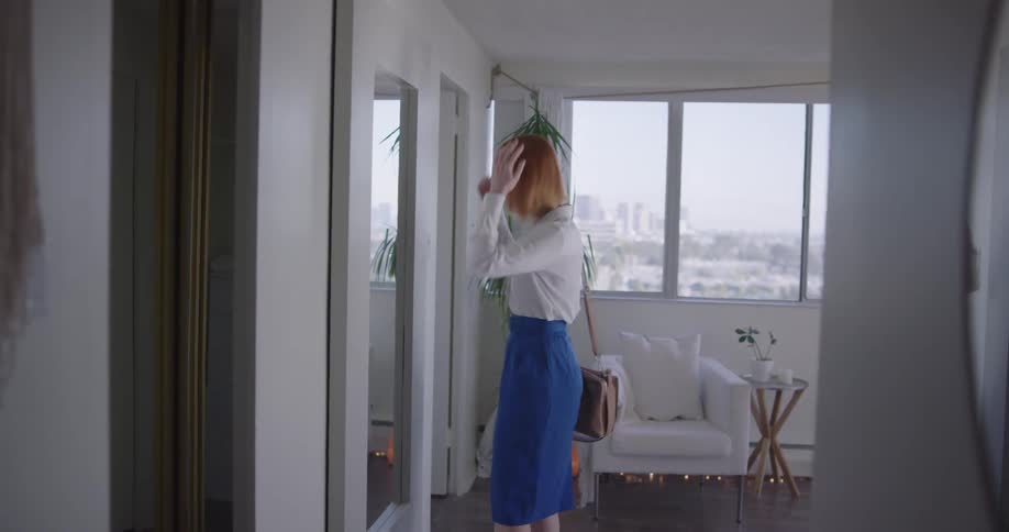 A woman checks her hair in a hallway mirror before leaving her house