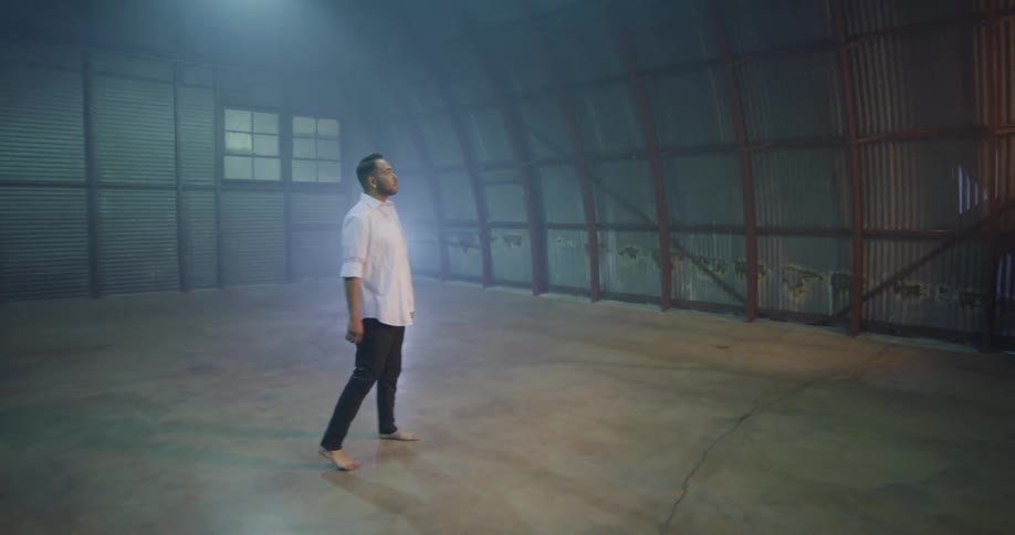 Man walks barefoot into empty building with concrete floor and stands looking around