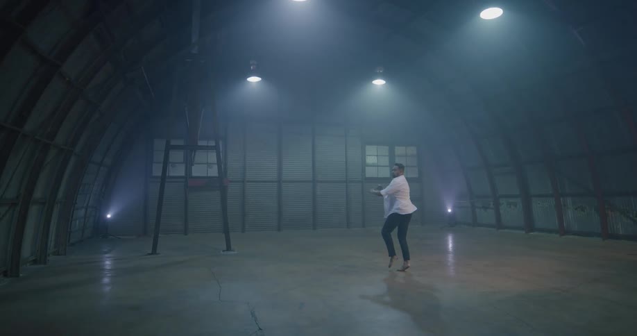 Man dances twirling andjumping in empty building with concrete floor
