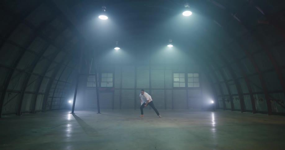 A man practices a modern dance in a large open hangar