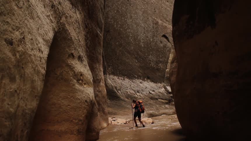 A hiker walks through a stream in a canyon