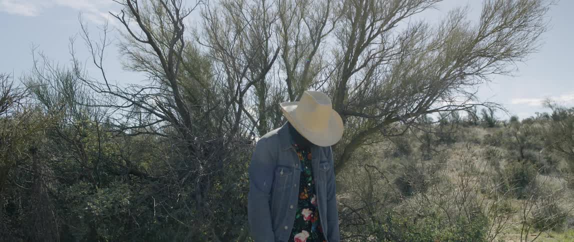 A man standing in a field dressed as a scarecrow drops his arms and head down
