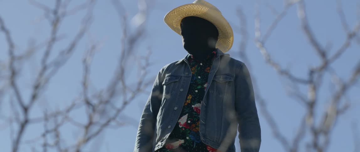 Man wearing face mask and cowboy hat stands on the desert at day