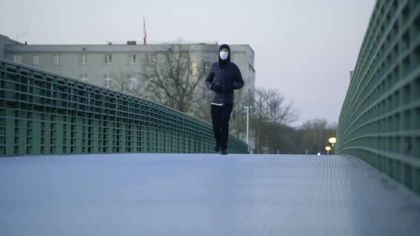 A man jogs across a bridge while wearing a face mask