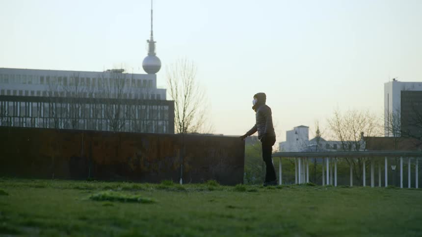 A person stands outside supporting themselves with a short wall as they stretch