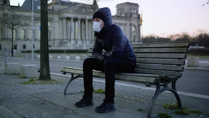 A young man wearing a mask sits on a bench