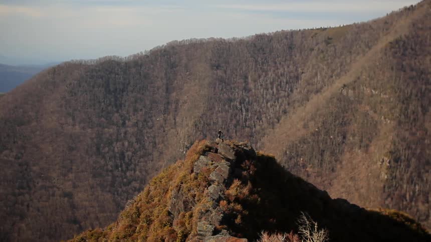 A person waves their arms on a mountain peak