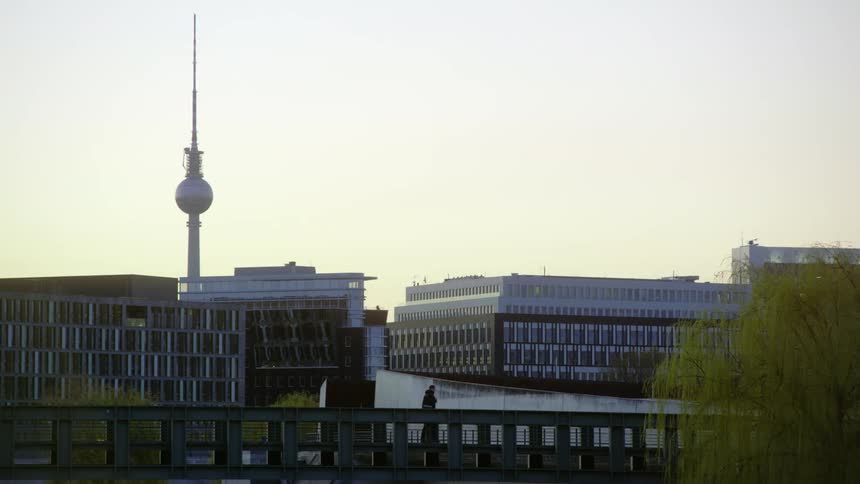 Person walks along bridge near buildings and spire