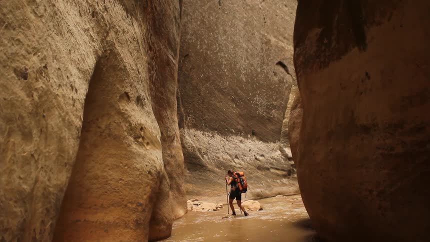 A man is hiking in between two very tall caverns on a sunny day